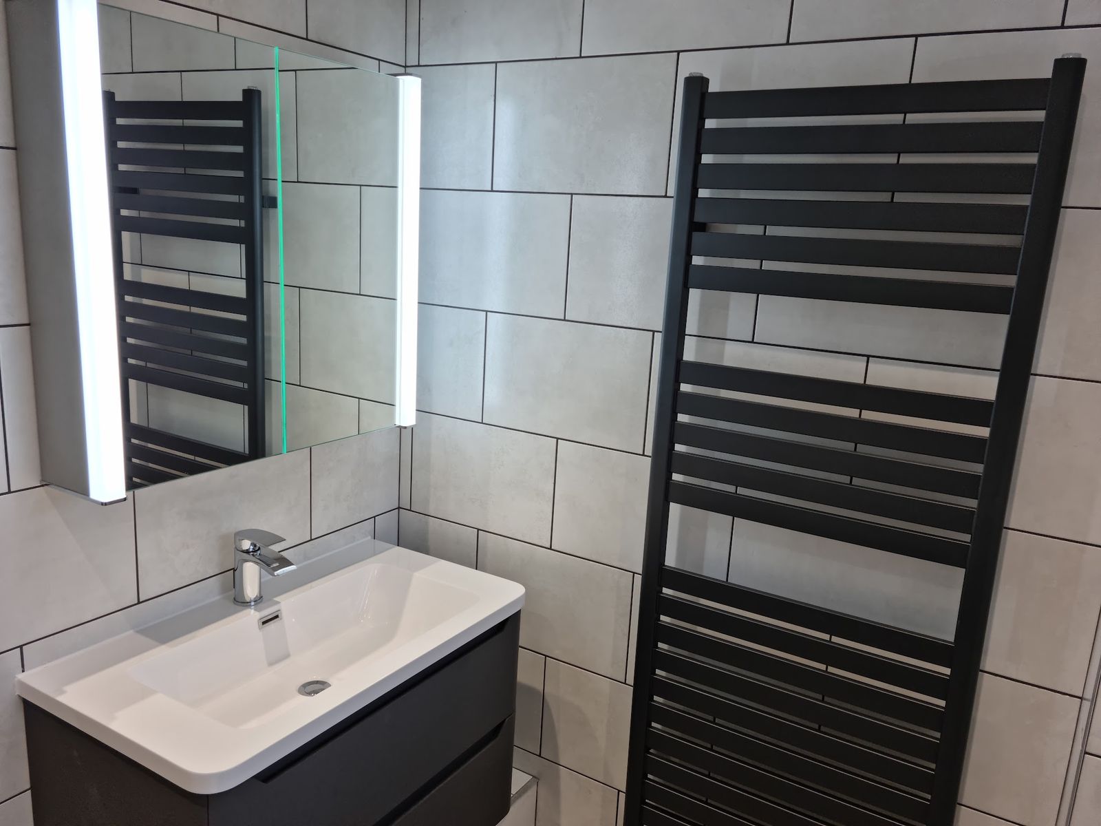 A vanity basin with a lit mirror and a black towel radiator