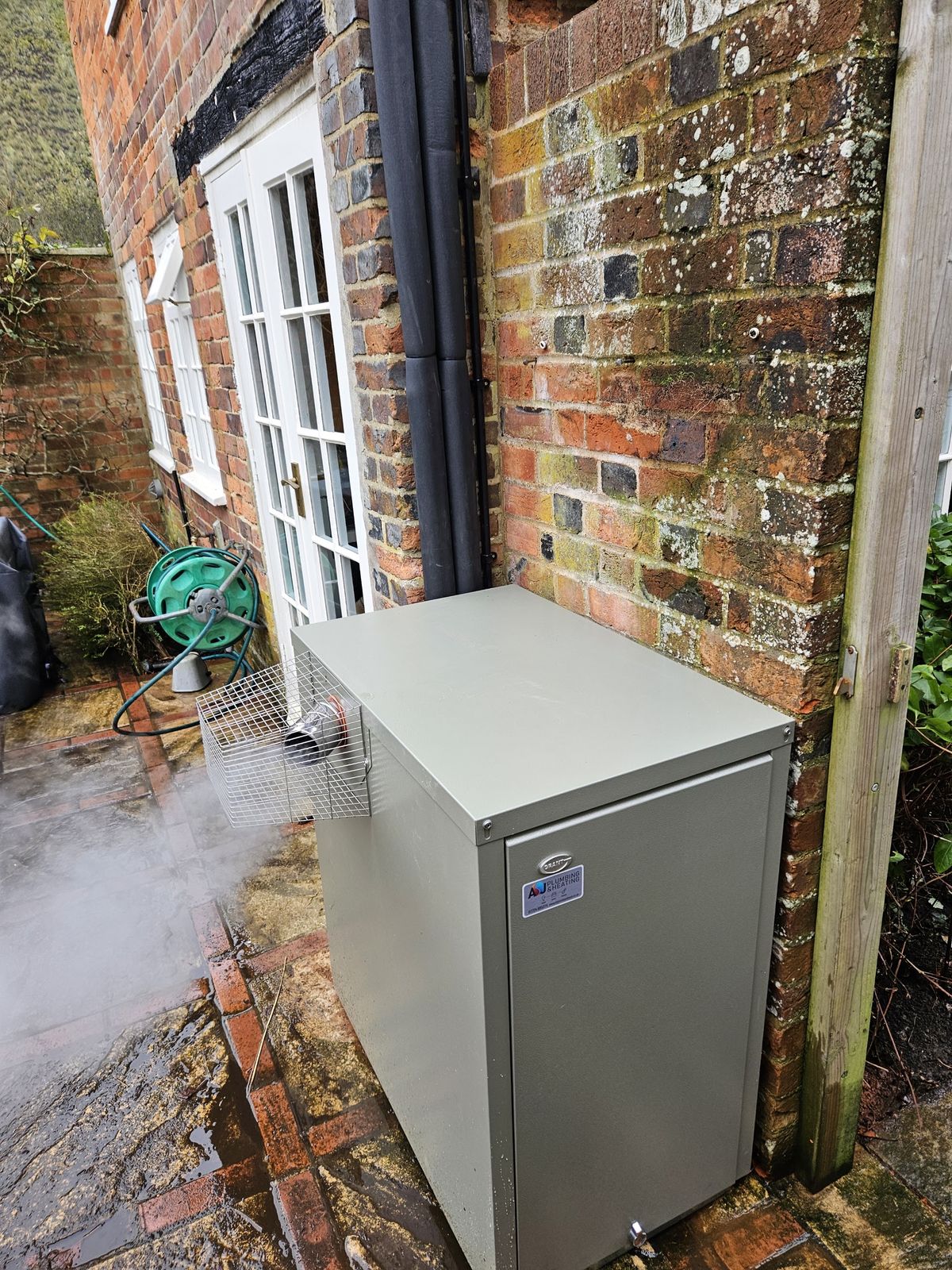 An outdoor oil boiler housing beside a brick cottage wall