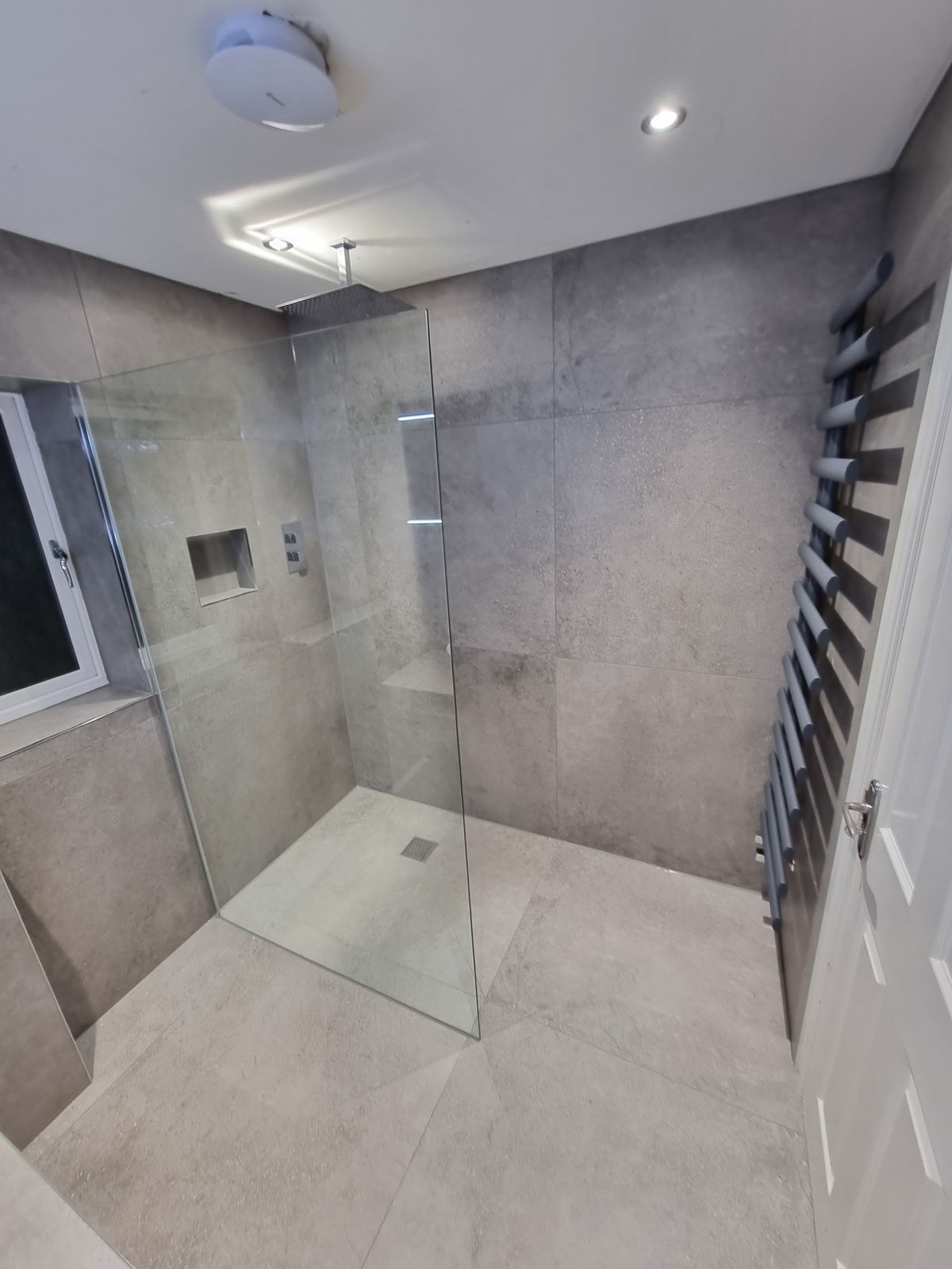 A walk-in wet room with a glass screen and large grey tiles