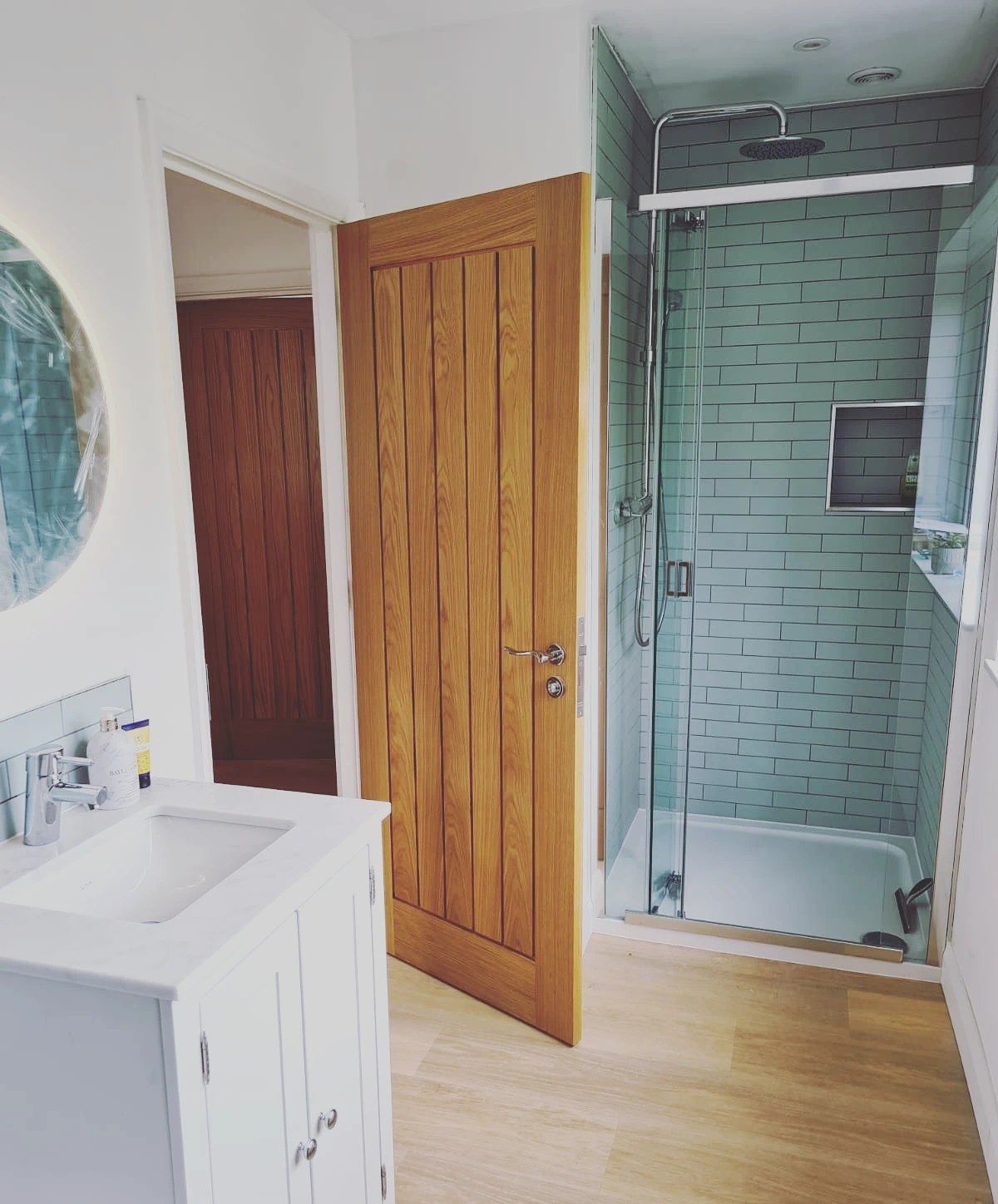 A bathroom with a walk-in shower, white vanity and oak door
