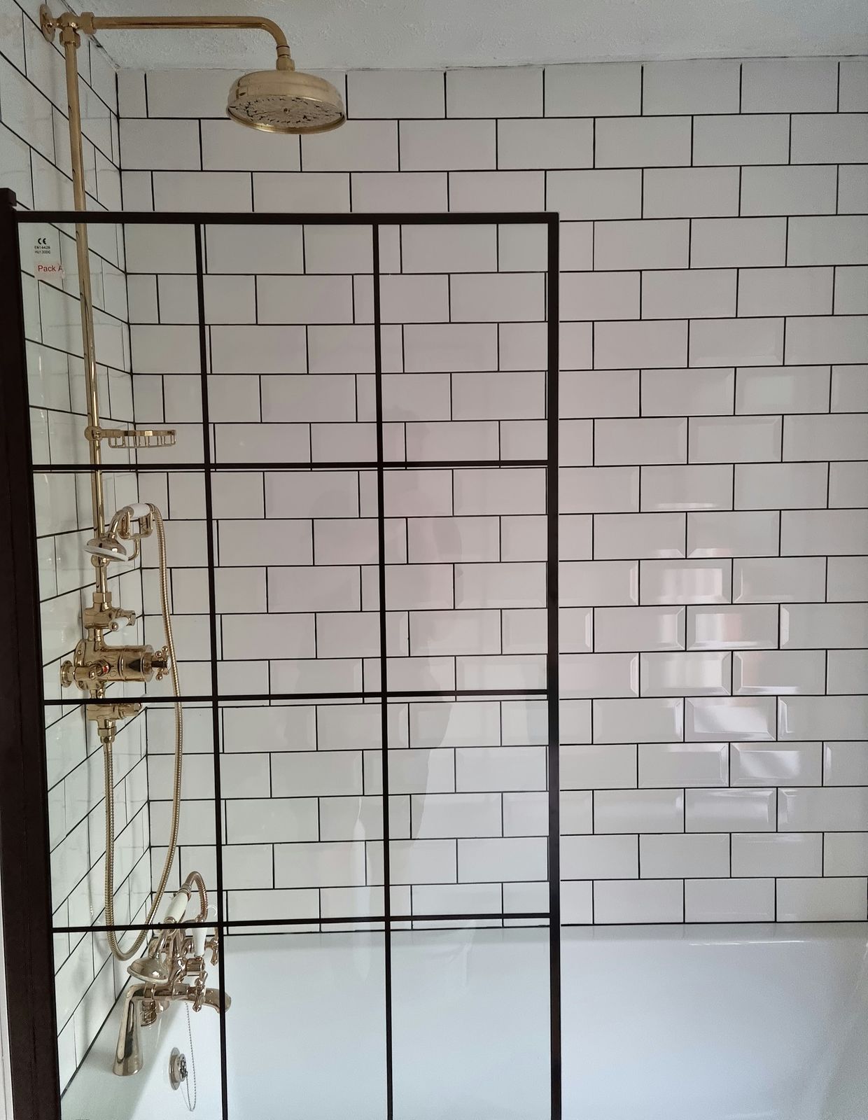 A black grid shower screen with brass fittings and white metro tiles