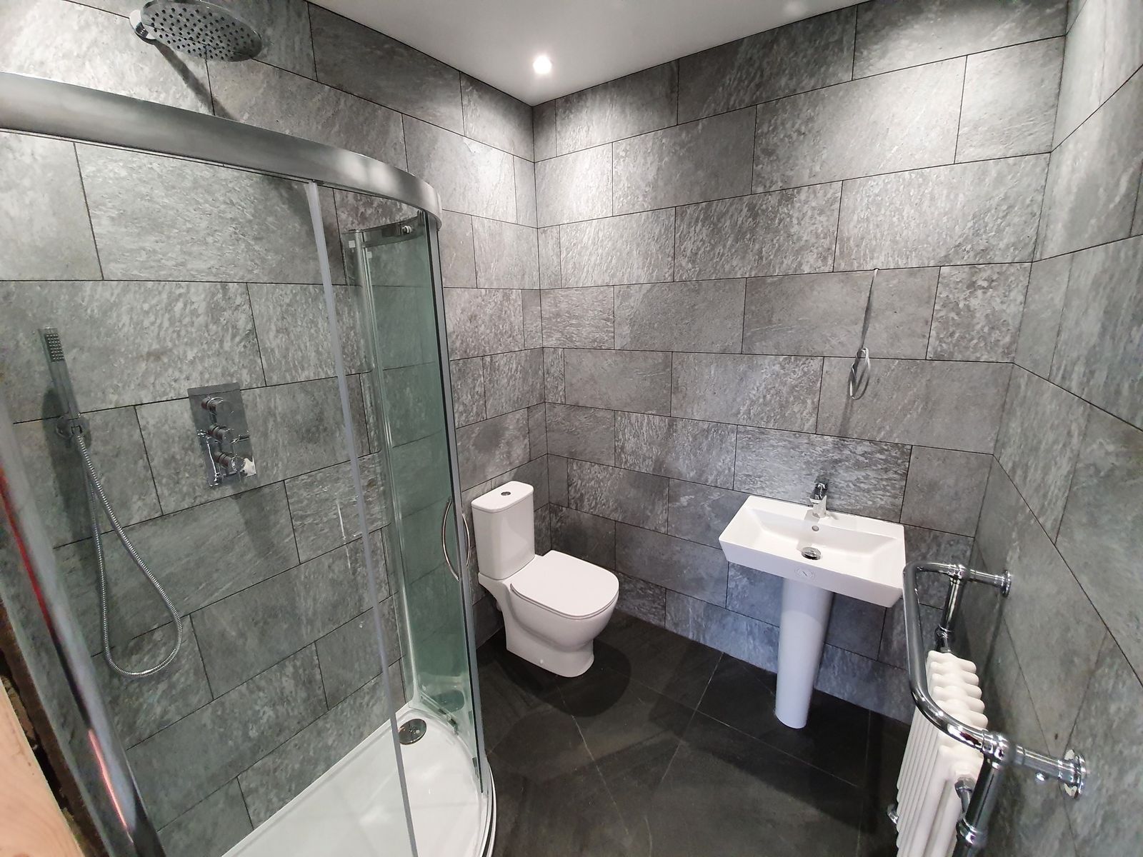 A grey tiled shower room with a quadrant enclosure