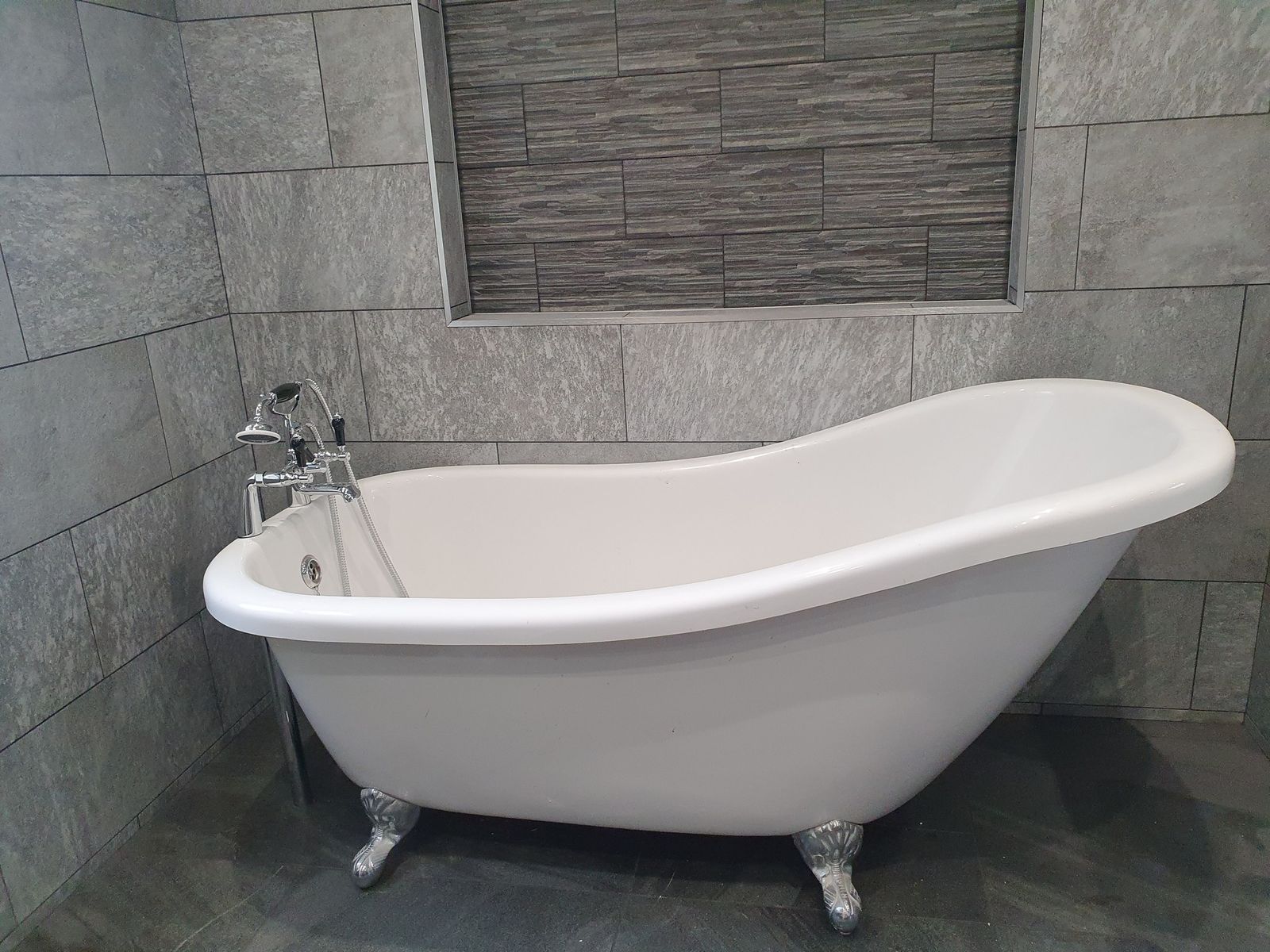 A freestanding slipper bath against grey tiles