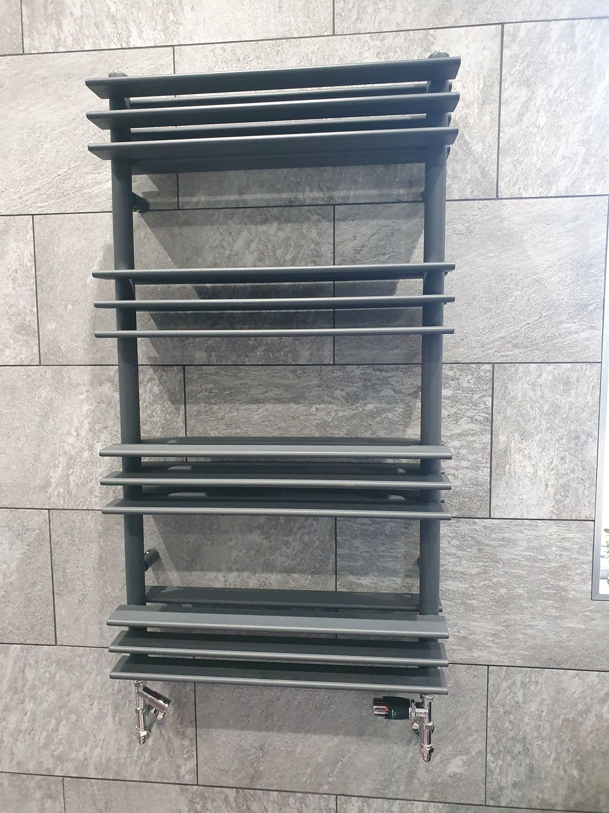 An anthracite towel radiator on grey tiles